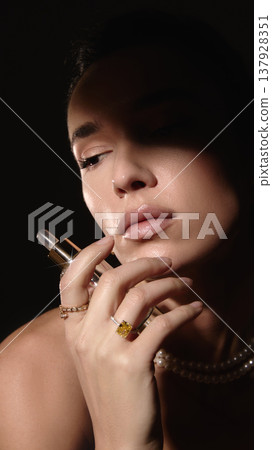 Woman holding cosmetic serum bottle with glowing skin in dark studio light. Woman holding cosmetic serum bottle with glowing skin in dark studio light. 137928351
