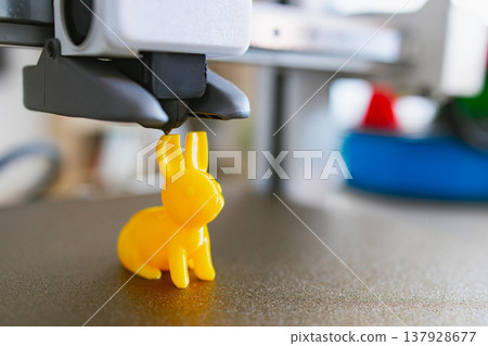 A yellow bunny figurine is being created by a 3D printer, showcasing additive manufacturing technology in action A yellow bunny figurine is being created by a 3D printer, showcasing additive manufacturing technology in action 137928677