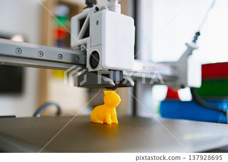 A close-up shot of a 3D printer extruding a small, bright yellow toy animal on its build plate A close-up shot of a 3D printer extruding a small, bright yellow toy animal on its build plate 137928695