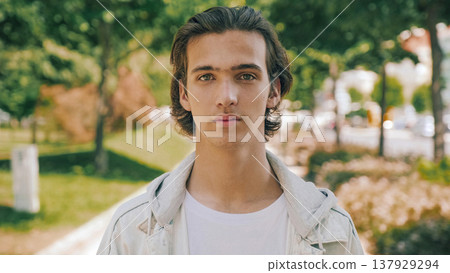 Closeup portrait of handsome confident young man at the park in summer. Confident teenager looks to the camera, outdoor portrait. Handsome face of a male model with brown hair at city. One person Closeup portrait of handsome confident young man at the park in summer. Confident teenager looks to the camera, outdoor portrait. Handsome face of a male model with brown hair at city. One person 137929294