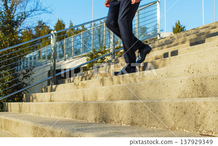 Businessman in black classic shoes and trousers runs going down the stairs. Unrecognized person - businessman in fashionable shoes walking down the steps. Businessman in black classic shoes and trousers runs going down the stairs. Unrecognized person - businessman in fashionable shoes walking down the steps. 137929349