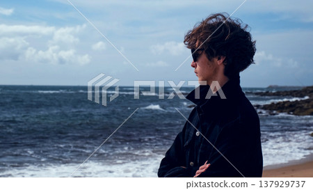 Young man stands on the empty sandy beach on the summer day and contemplating ocean water surface. Human stands on beach on a sunny day and looking to distance. Young man stands on the empty sandy beach on the summer day and contemplating ocean water surface. Human stands on beach on a sunny day and looking to distance. 137929737