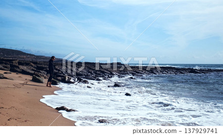 On a hot summer day, a young man wanders barefoot on an empty sandy beach. On a beautiful day, a man walks along a sandy beach. A man in an amorous mood on the beach, admiring nature's beauty.. On a hot summer day, a young man wanders barefoot on an empty sandy beach. On a beautiful day, a man walks along a sandy beach. A man in an amorous mood on the beach, admiring nature's beauty.. 137929741