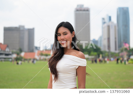 Cute woman smiling outdoors at Merdeka Square with Kuala Lumpur city skyline and a green park field Cute woman smiling outdoors at Merdeka Square with Kuala Lumpur city skyline and a green park field 137931060
