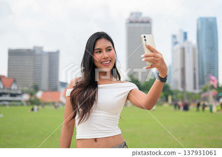 Cute woman smiling outdoors at Merdeka Square with Kuala Lumpur city skyline and a green park field Cute woman smiling outdoors at Merdeka Square with Kuala Lumpur city skyline and a green park field 137931061