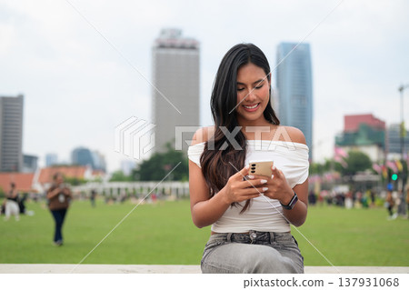 Cute woman smiling outdoors at Merdeka Square with Kuala Lumpur city skyline and a green park field Cute woman smiling outdoors at Merdeka Square with Kuala Lumpur city skyline and a green park field 137931068