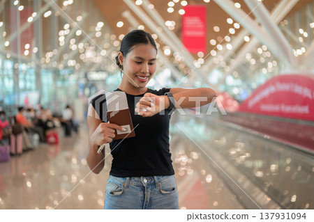 Young woman standing in airport terminal using phone and holding a passport with a boarding pass Young woman standing in airport terminal using phone and holding a passport with a boarding pass 137931094