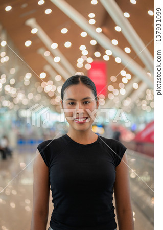 A portrait of a smiling young Asian woman wearing a black t-shirt in a modern airport terminal 137931099
