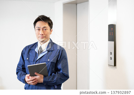A male facility manager holding a tablet in the elevator lobby. 137932897