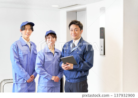 A facility management leader and a young male and female worker holding tablets in the elevator lobby. A facility management leader and a young male and female worker holding tablets in the elevator lobby. 137932900