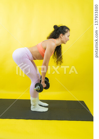 Woman training deadlift with dumbbells on exercise mat 137933880
