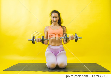 Woman exercising biceps with dumbbells on mat Woman exercising biceps with dumbbells on mat 137933936
