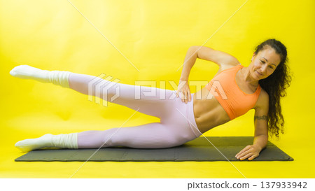 Woman performing side leg raise exercise on exercise mat Woman performing side leg raise exercise on exercise mat 137933942