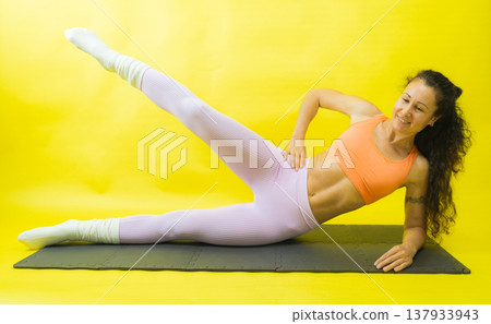 Woman performing side leg lift exercise on mat Woman performing side leg lift exercise on mat 137933943