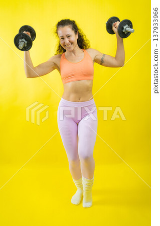 Woman smiling lifting dumbbells during fitness workout Woman smiling lifting dumbbells during fitness workout 137933966