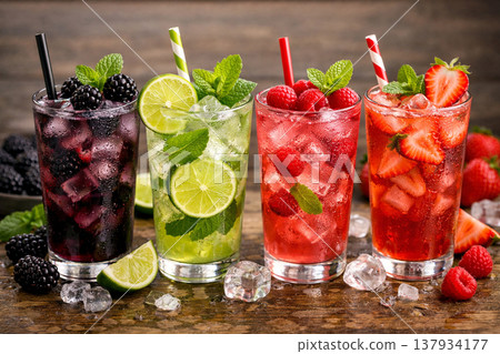 Four refreshing summer cocktails in glasses filled with ice, featuring blackberry, lime, raspberry, and strawberry flavors, garnished with fresh mint on a rustic wooden background 137934177