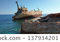 Tourist sitting on a rocky cliff watching the grounded rusty cargo ship EDRO III against the clear blue sky and turquoise Mediterranean Sea near Paphos, Cyprus 137934201