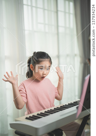 Young Girl Expressing Surprise While Playing Keyboard in Bright Room with Natural Light and Soft Curtains Young Girl Expressing Surprise While Playing Keyboard in Bright Room with Natural Light and Soft Curtains 137934234
