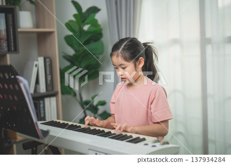 Young Girl Playing Keyboard at Home with Natural Light and Indoor Plants in a Cozy Living Room Setting 137934284