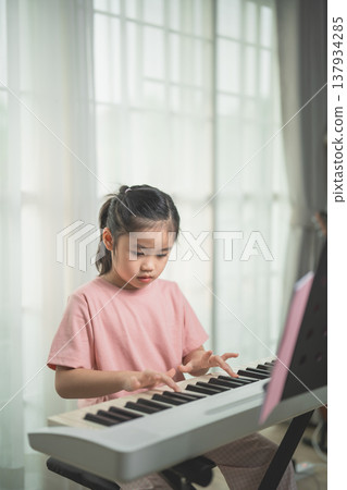 Young Girl Playing Keyboard in a Cozy Room Filled with Natural Light, Showcasing Passion for Music and Creativity Through Artistic Expression 137934285
