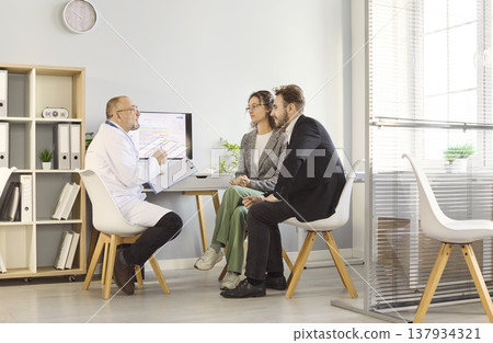 Doctor consulting couple in modern clinic, seated meeting about test results Doctor consulting couple in modern clinic, seated meeting about test results 137934321