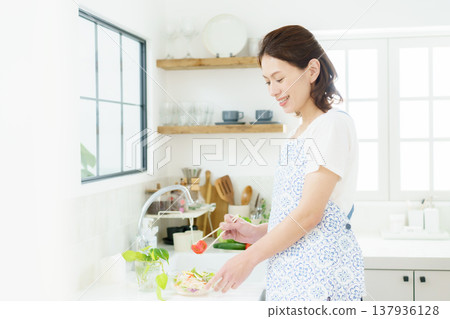 A smiling middle-aged housewife making a salad in the kitchen. 137936128