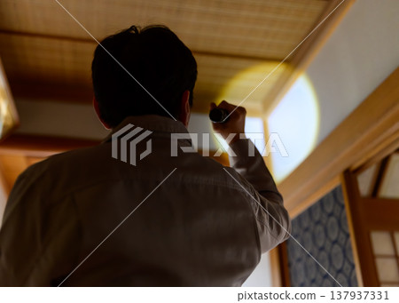 The back view of a man illuminating a dark room with a flashlight. The back view of a man illuminating a dark room with a flashlight. 137937331
