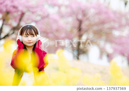 一位年輕女子在櫻花樹下戴著耳機聽音樂。 一位年輕女子在櫻花樹下戴著耳機聽音樂。 137937369