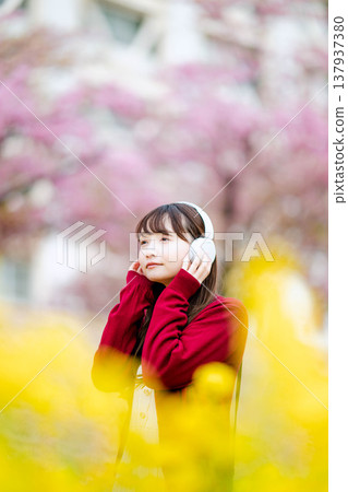 一位年輕女子在櫻花樹下戴著耳機聽音樂。 一位年輕女子在櫻花樹下戴著耳機聽音樂。 137937380