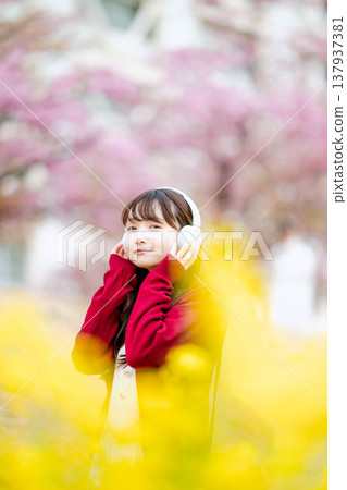 一位年輕女子在櫻花樹下戴著耳機聽音樂。 137937381
