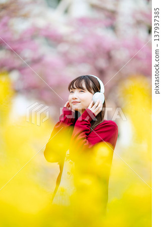 一位年輕女子在櫻花樹下戴著耳機聽音樂。 137937385