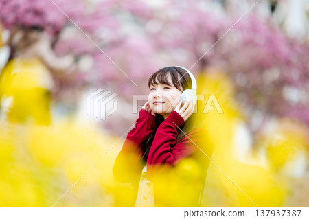 一位年輕女子在櫻花樹下戴著耳機聽音樂。 一位年輕女子在櫻花樹下戴著耳機聽音樂。 137937387
