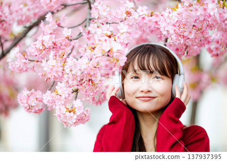 一位年輕女子在櫻花樹下戴著耳機聽音樂。 137937395