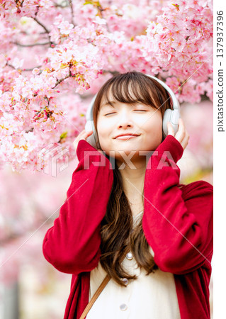 一位年輕女子在櫻花樹下戴著耳機聽音樂。 一位年輕女子在櫻花樹下戴著耳機聽音樂。 137937396
