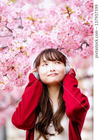 一位年輕女子在櫻花樹下戴著耳機聽音樂。 137937399