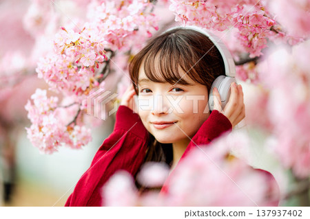 一位年輕女子在櫻花樹下戴著耳機聽音樂。 137937402