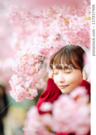 一位年輕女子在櫻花樹下戴著耳機聽音樂。 137937406