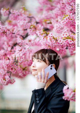 一位年輕女子在櫻花樹下用智慧型手機通話。 一位年輕女子在櫻花樹下用智慧型手機通話。 137937590