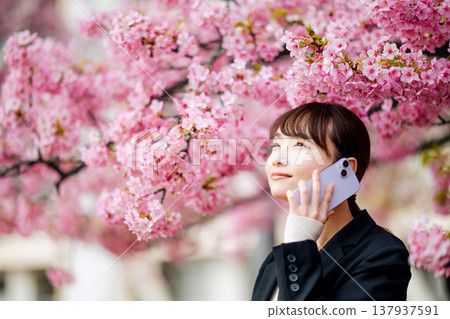 一位年輕女子在櫻花樹下用智慧型手機通話。 一位年輕女子在櫻花樹下用智慧型手機通話。 137937591