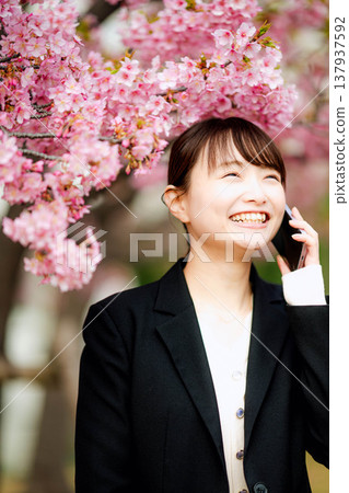 一位年輕女子在櫻花樹下用智慧型手機通話。 137937592