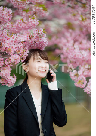 A young woman talking on her smartphone in front of cherry blossoms. A young woman talking on her smartphone in front of cherry blossoms. 137937594