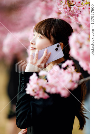 一位年輕女子在櫻花樹下用智慧型手機通話。 137937600