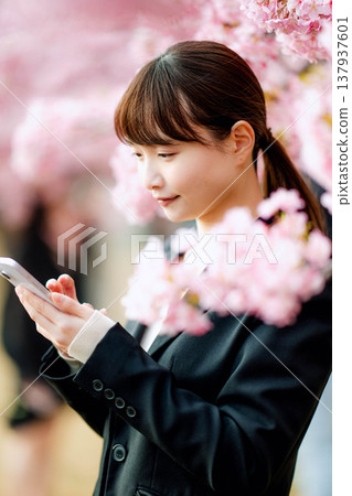 一位年輕女子在櫻花樹下用智慧型手機通話。 一位年輕女子在櫻花樹下用智慧型手機通話。 137937601