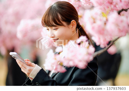 A young woman talking on her smartphone in front of cherry blossoms. A young woman talking on her smartphone in front of cherry blossoms. 137937603