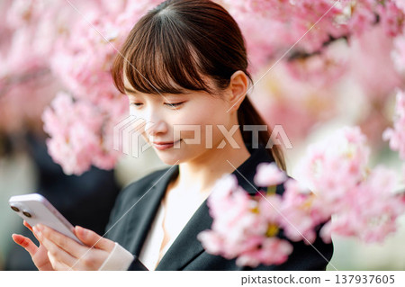 一位年輕女子在櫻花樹下用智慧型手機通話。 一位年輕女子在櫻花樹下用智慧型手機通話。 137937605