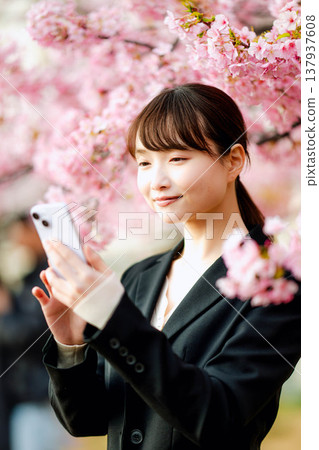 一位年輕女子在櫻花樹下用智慧型手機通話。 137937608