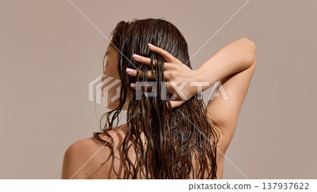 Woman touching wet curly hair from back view in studio. 137937622