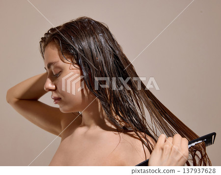 Woman combing wet curly hair with conditioner in studio Woman combing wet curly hair with conditioner in studio 137937628