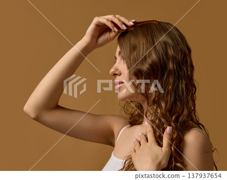 Woman combing curly hair with wooden comb in studio. Woman combing curly hair with wooden comb in studio. 137937654