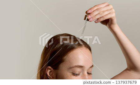 Woman applying serum to scalp with dropper in studio close up. Woman applying serum to scalp with dropper in studio close up. 137937679